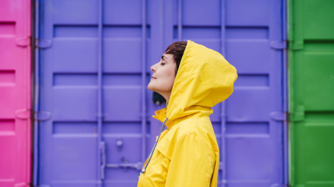 portrait of relaxed caucasian woman wearing yellow raincoat, standing with eyes closed over purple background. Lifestyle outdoors